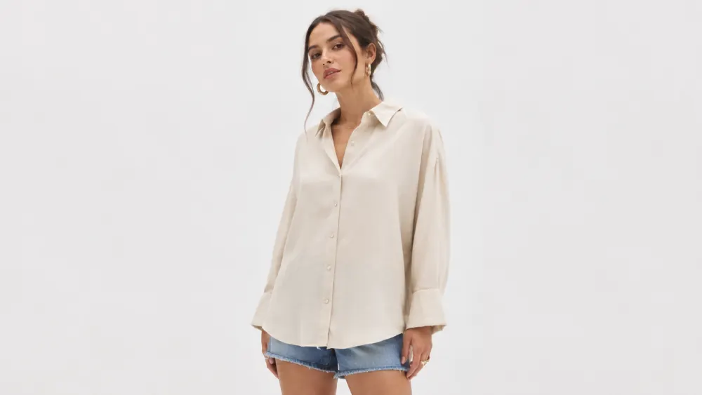 Mulher usando camisa bege de manga longa, solta e com punhos largos, com short jeans
