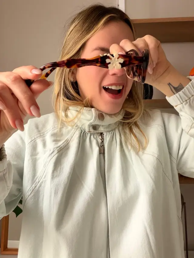 Brenda segurando os óculos de sol Nara, da coleção Farm x Zerezes, em acetato tartaruga com uma flor na haste